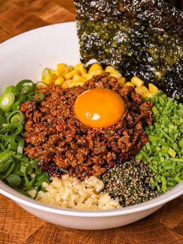 Spicy minced beef rice bowl with egg yolk and vegetables.