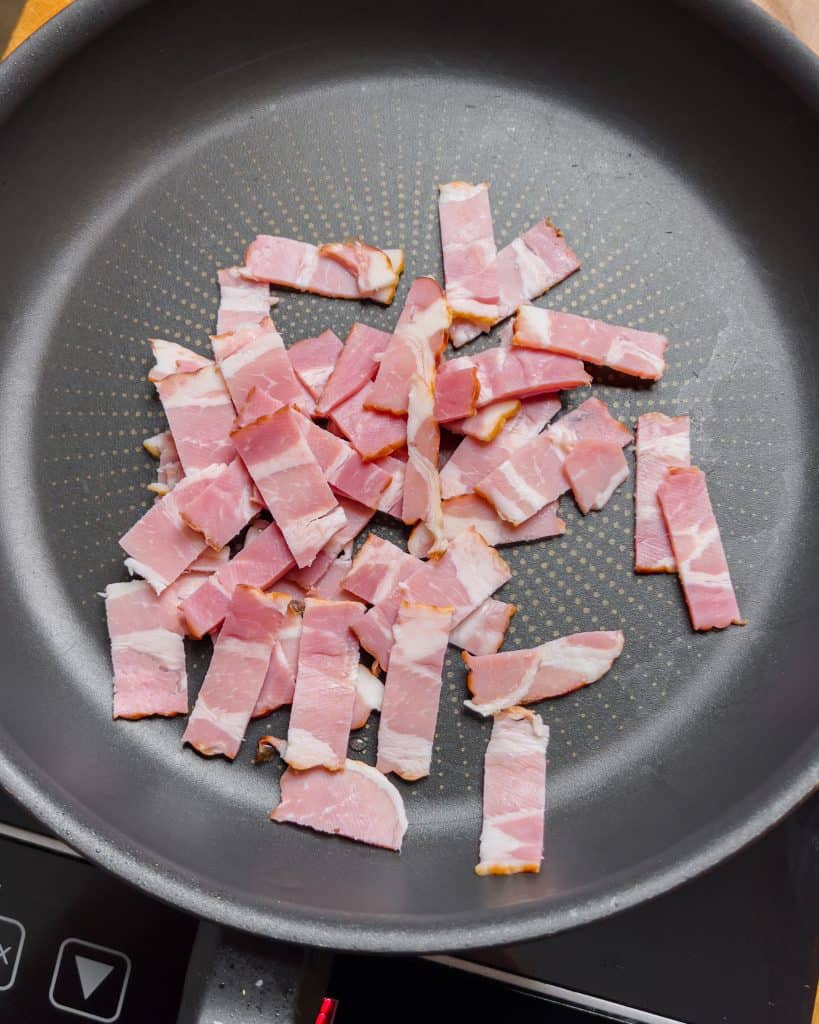 Bacon pieces in a pan, starting to cook