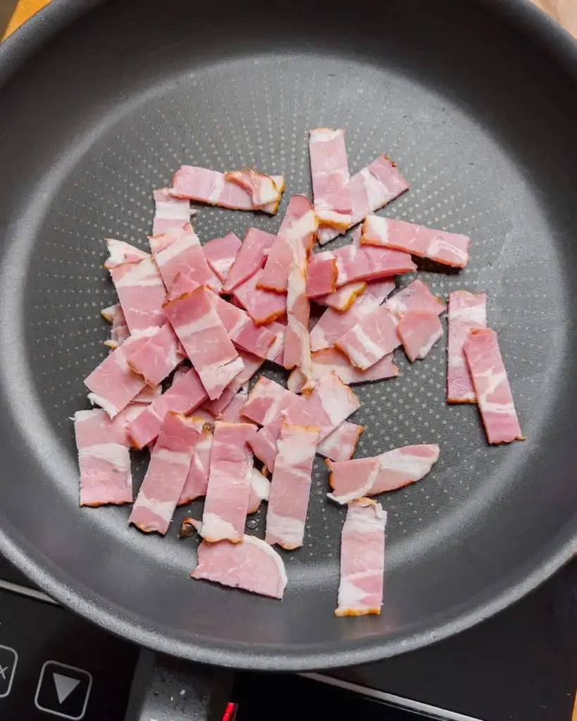 Bacon pieces in a pan, starting to cook - GENIUS EATS Bacon pieces in a pan, starting to cook