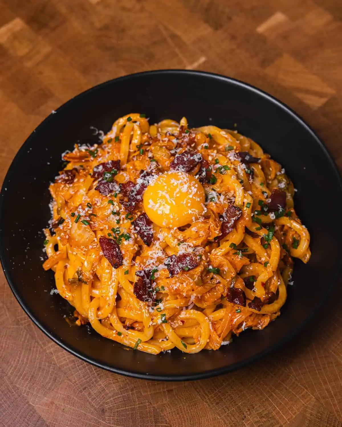 Creamy bacon pasta topped with egg yolk in a black bowl. - GENIUS EATS Cooking with kimchi