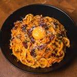 Creamy bacon pasta topped with egg yolk in a black bowl.