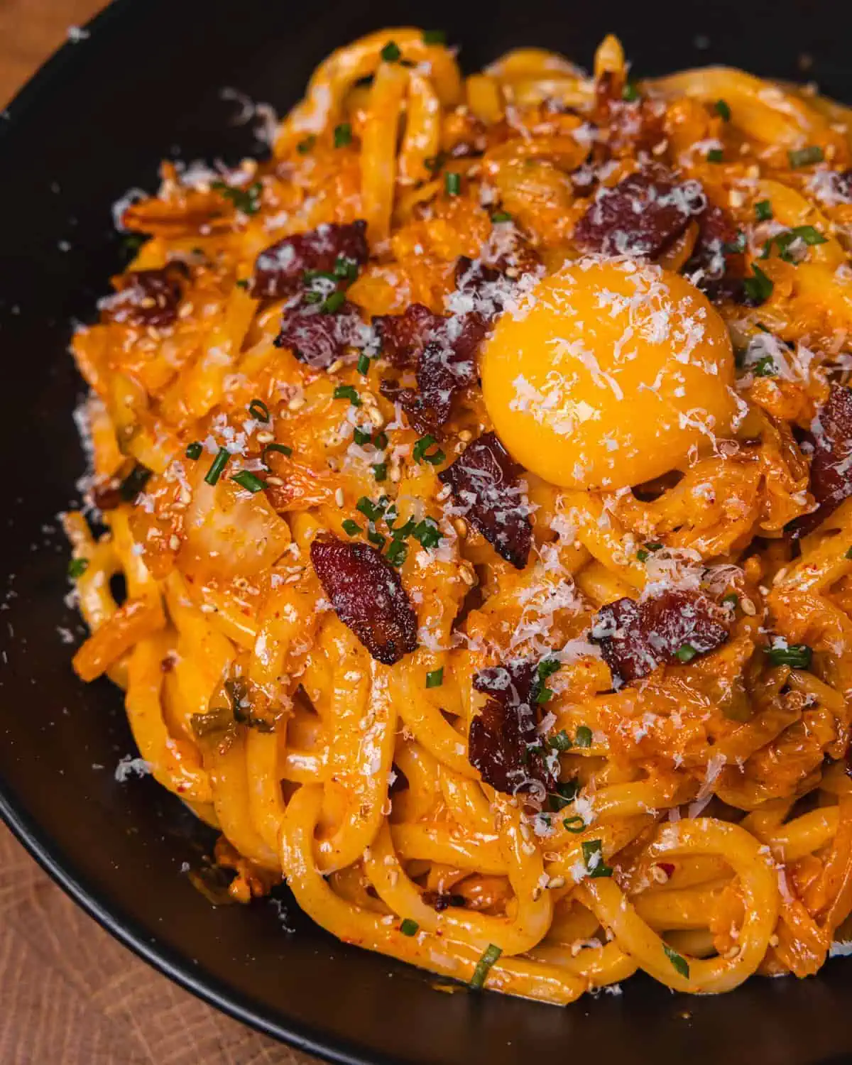 Creamy bacon pasta topped with egg yolk in a black bowl. - GENIUS EATS Creamy udon noodle dish