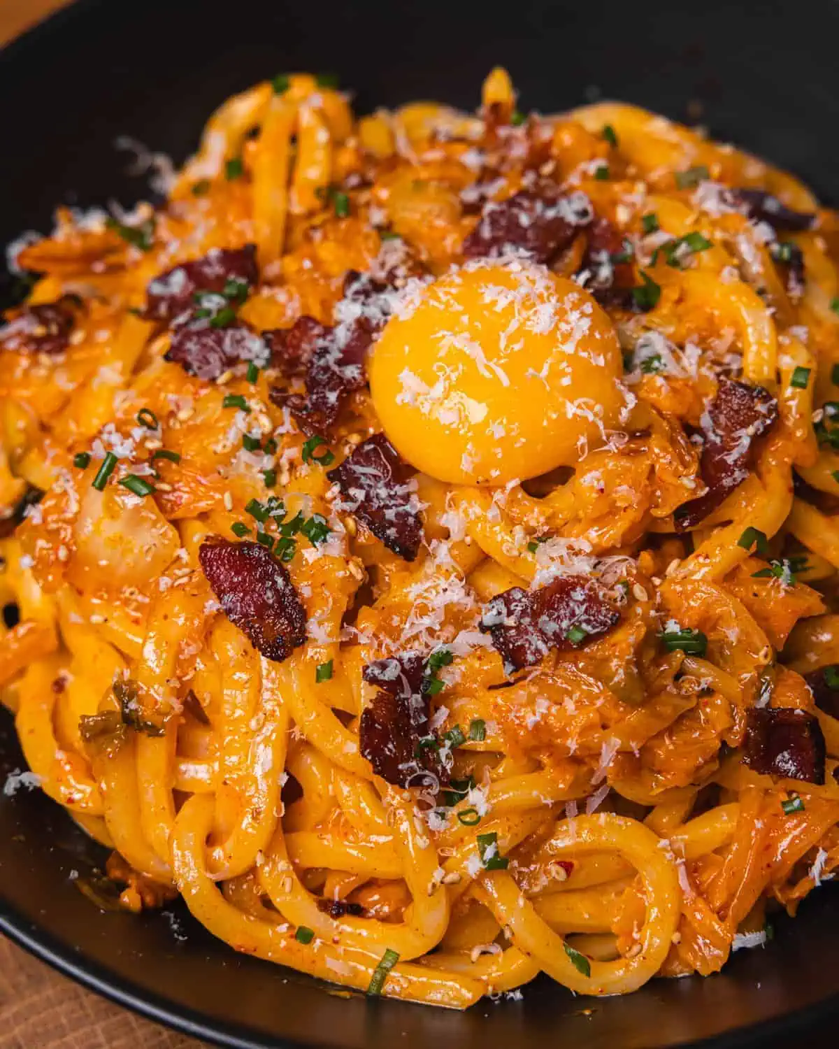 Creamy bacon pasta topped with egg yolk in a black bowl. - GENIUS EATS Easy kimchi noodles