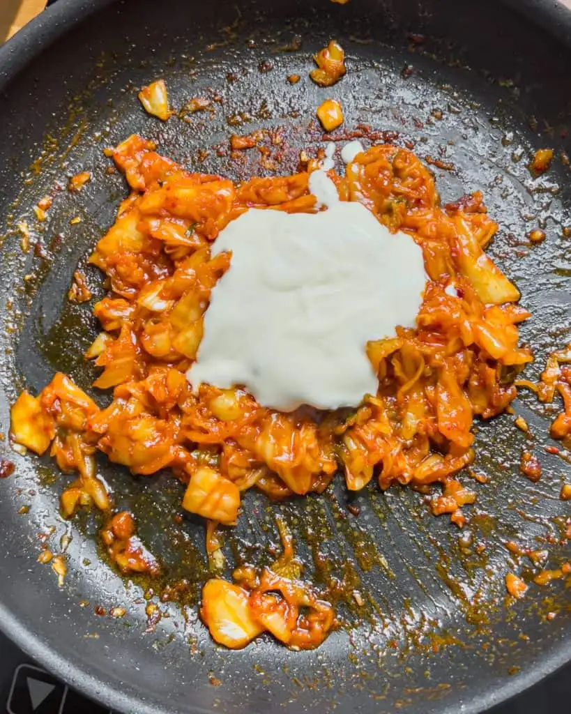 Heavy cream added to cooked kimchi in the pan. - GENIUS EATS Heavy cream added to cooked kimchi in the pan.