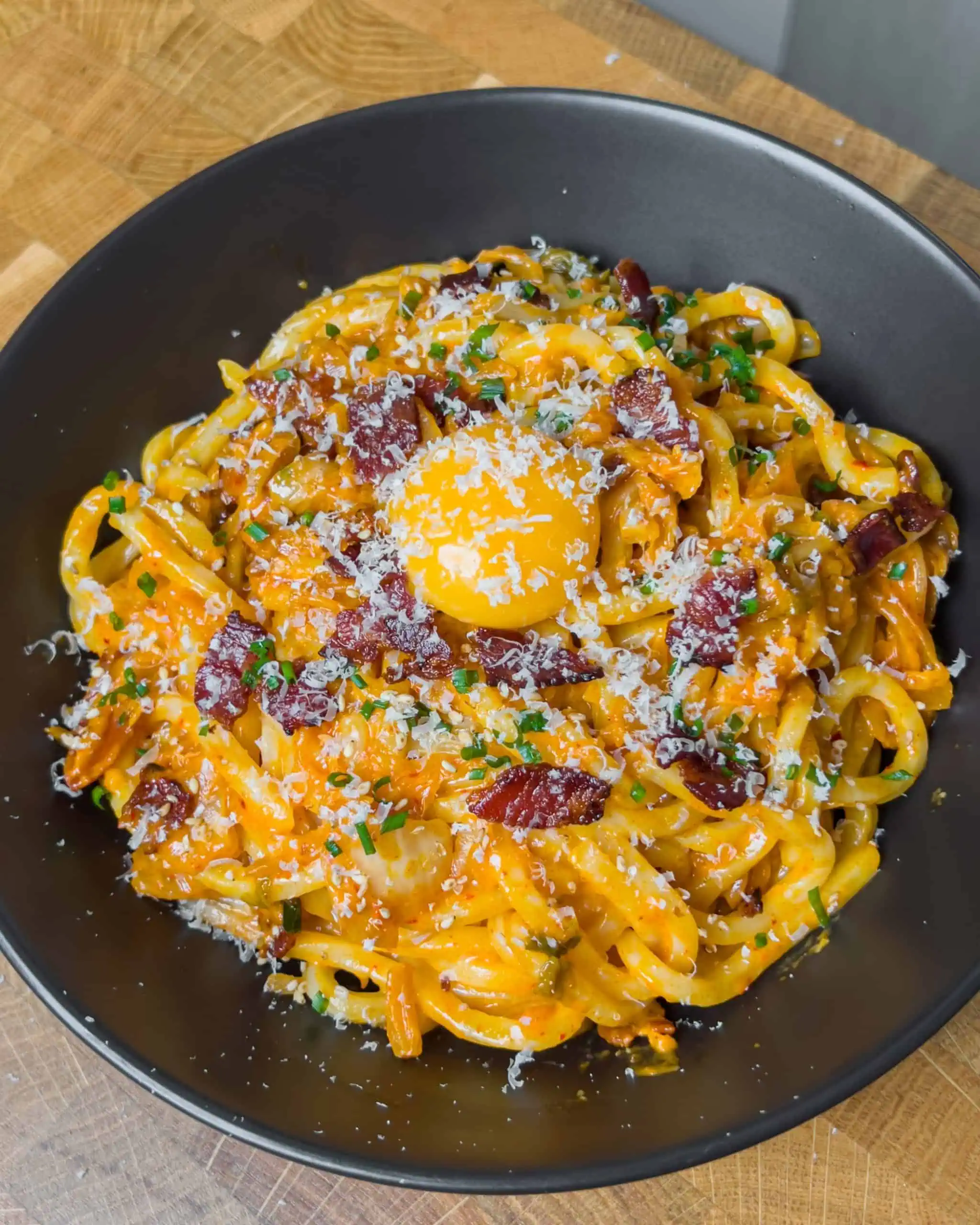 Udon noodles garnished with chives, sesame seeds, grated parmesan cheese, and egg yolk. - GENIUS EATS Udon noodles garnished with chives, sesame seeds, grated parmesan cheese, and egg yolk.