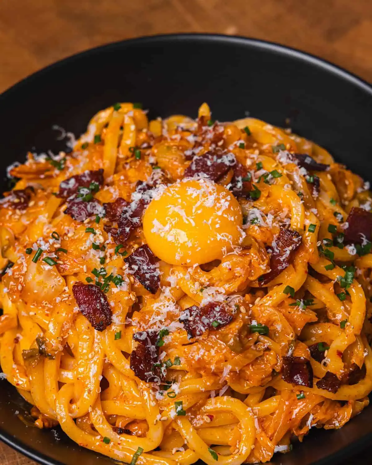 Creamy bacon pasta topped with egg yolk in a black bowl. - GENIUS EATS Vegetarian kimchi udon