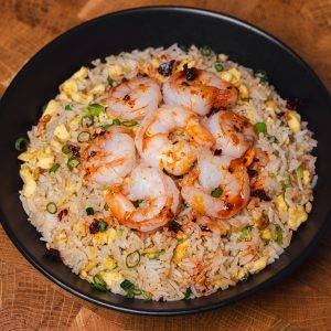 Shrimp fried rice in a bowl with shrimp, scrambled eggs, green onions, and chili oil garnish