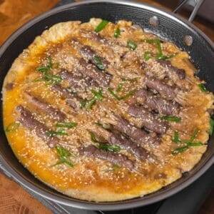 Beef enoki rolls simmered in savory sauce with sesame and scallions