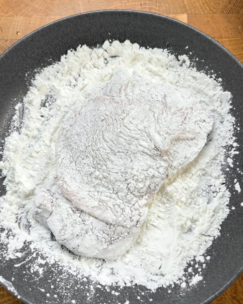 Chicken thighs coated in a fine layer of white cornstarch in a black bowl - GENIUS EATS Chicken thighs coated in a fine layer of white cornstarch in a black bowl