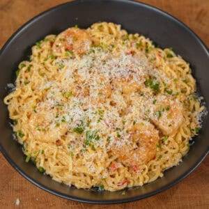 Creamy shrimp ramen topped with Parmesan and herbs in a black bowl.