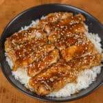 Glazed sesame chicken slices served over steamed rice in a bowl.