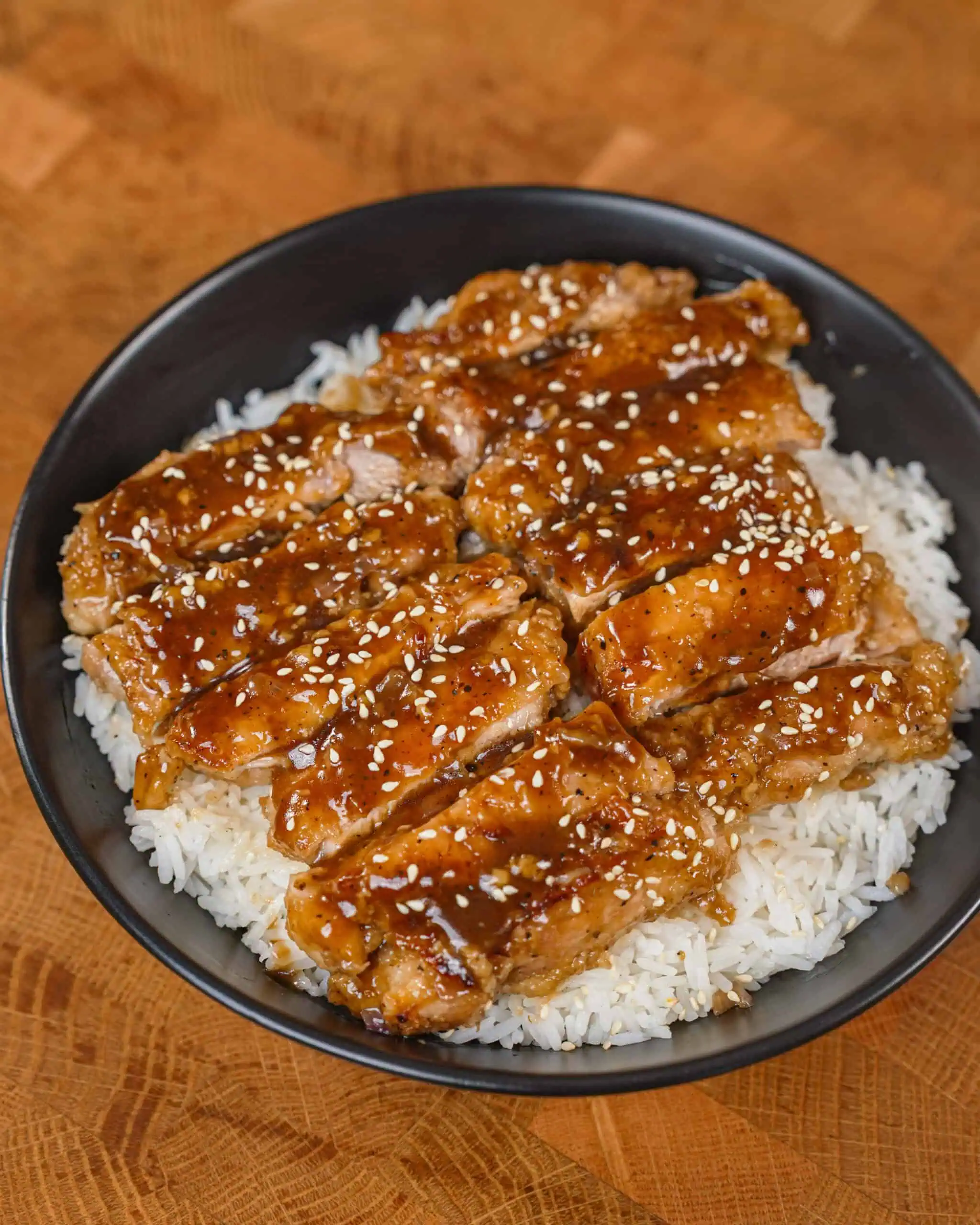 Glazed sesame chicken slices served over steamed rice in a bowl. - GENIUS EATS Crispy chicken with black pepper marinade