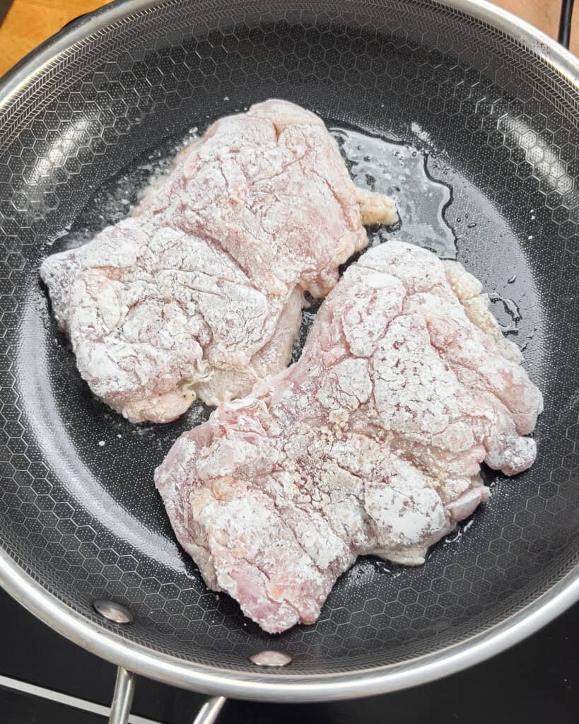 Dredged chicken thighs placed skin-side down in a hot skillet
