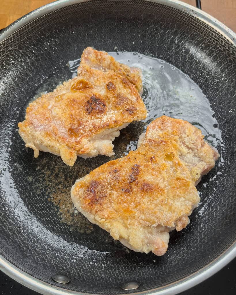 Golden-brown crisped chicken thighs cooking in the pan