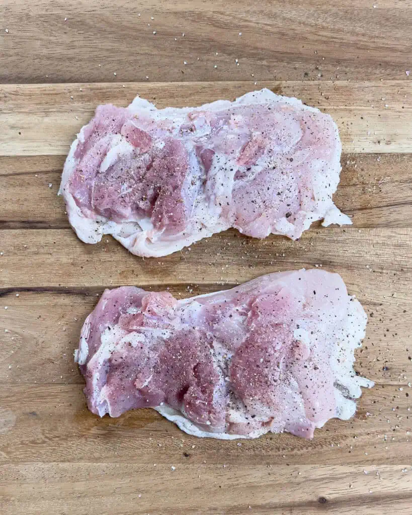 Raw chicken thighs seasoned with salt and black pepper on a wooden cutting board - GENIUS EATS Raw chicken thighs seasoned with salt and black pepper on a wooden cutting board