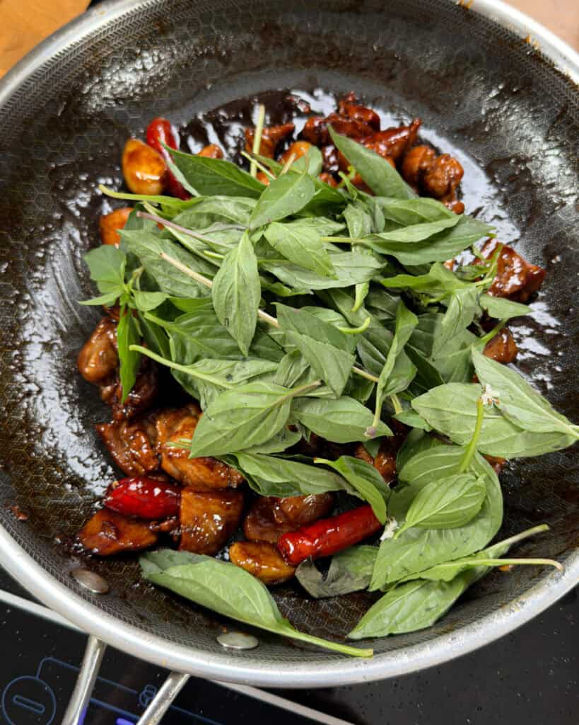 Fresh Thai basil leaves added to caramelized chicken in a wok