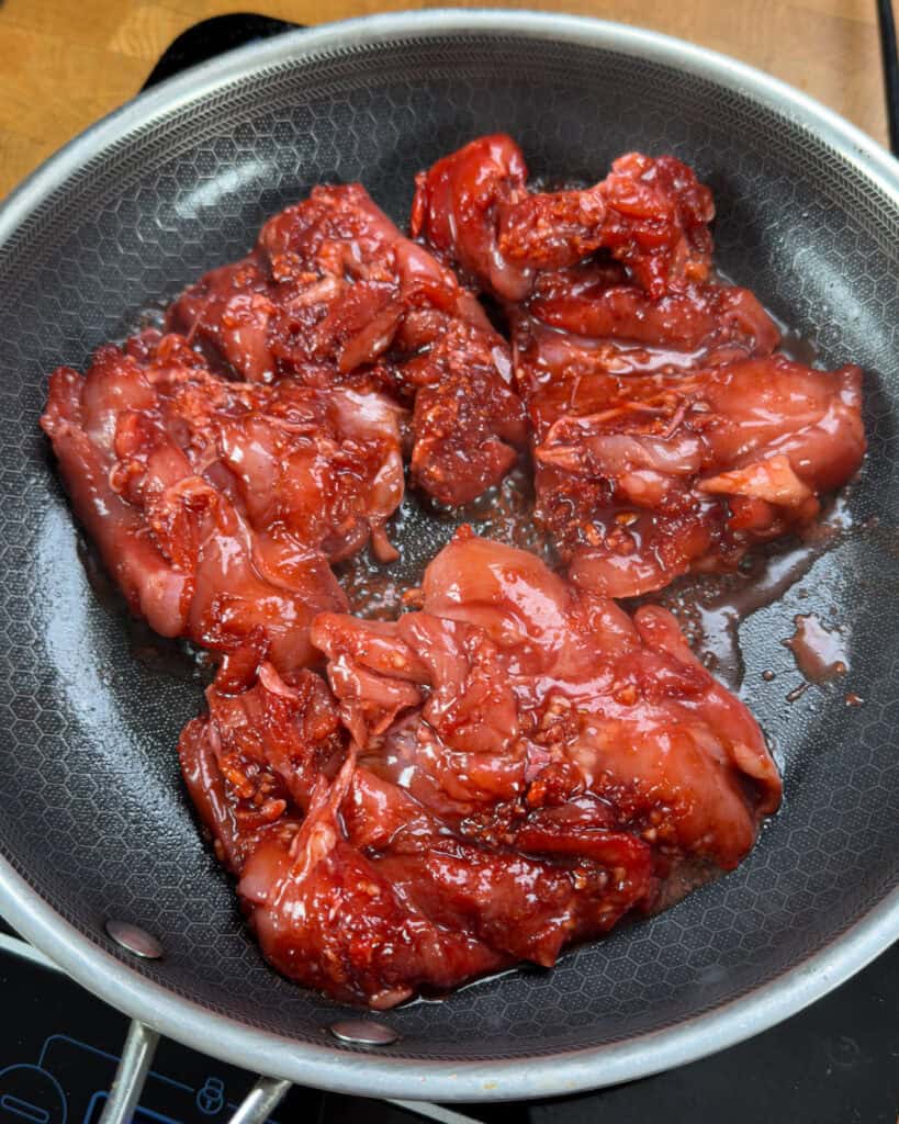 Marinated chicken added to a hot pan starting to sear and sizzle