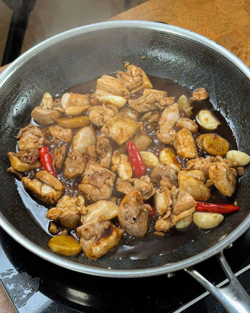 Partially browned chicken simmering with aromatics in sesame oil