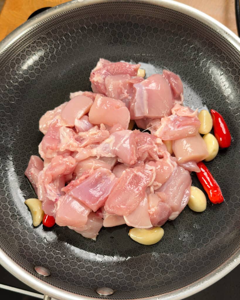 Raw chicken chunks cooking with garlic ginger and chili in a wok