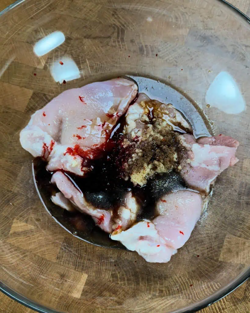 Raw chicken in a glass bowl with soy sauce garlic hoisin and honey marinade ingredients before mixing - GENIUS EATS Raw chicken in a glass bowl with soy sauce garlic hoisin and honey marinade ingredients before mixing