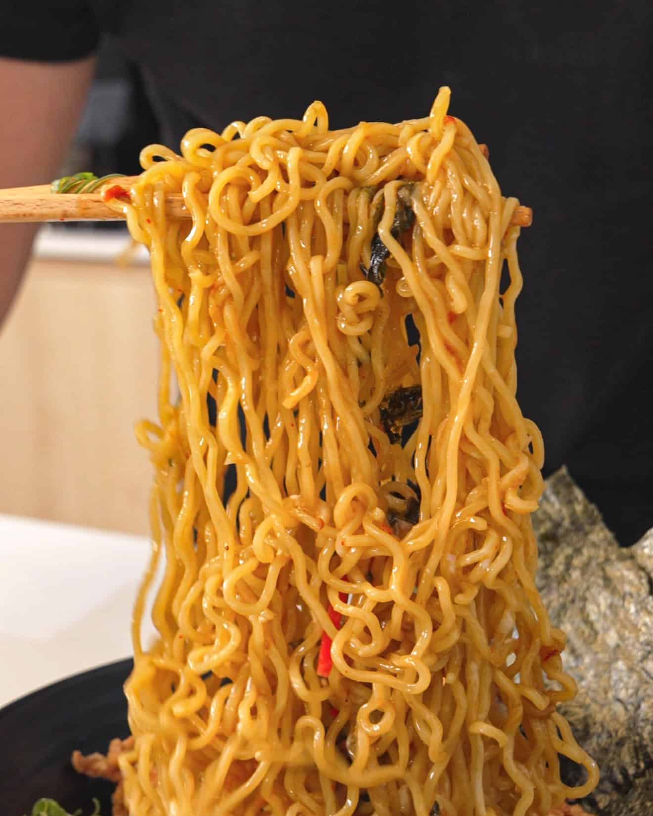 Close-up of stir-fried noodles with vegetables, served with seaweed in the background.