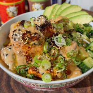 Tasty chicken bowl with avocado, green onions, and sesame seeds, served in a decorative bowl.