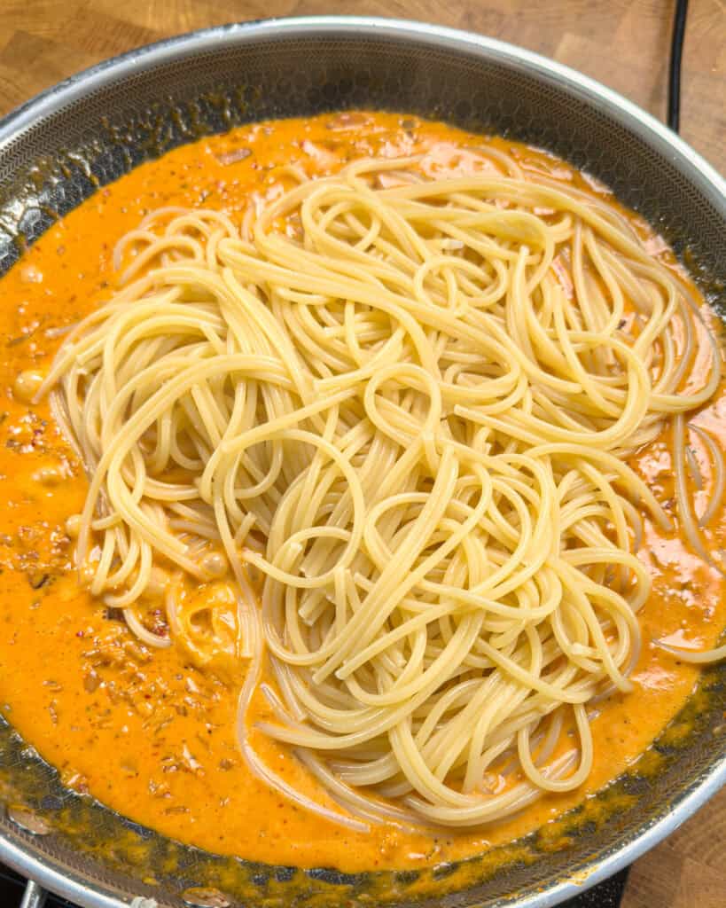 Cooked spaghetti strands added into orange sauce