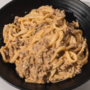 Creamy beef stroganoff with noodles in a black bowl, delicious comfort food.