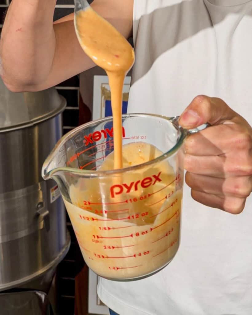 Creamy orange bang bang sauce dripping from spoon in measuring cup
