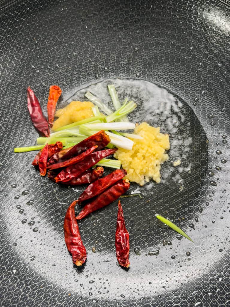 Dried red chilies ginger garlic and onions frying in oil for Kung Pao Chicken