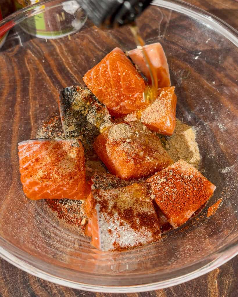 Liquid being added to raw salmon cubes in a bowl