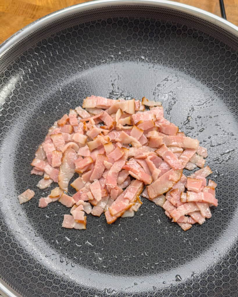 Raw bacon pieces spread in pan at the start of cooking