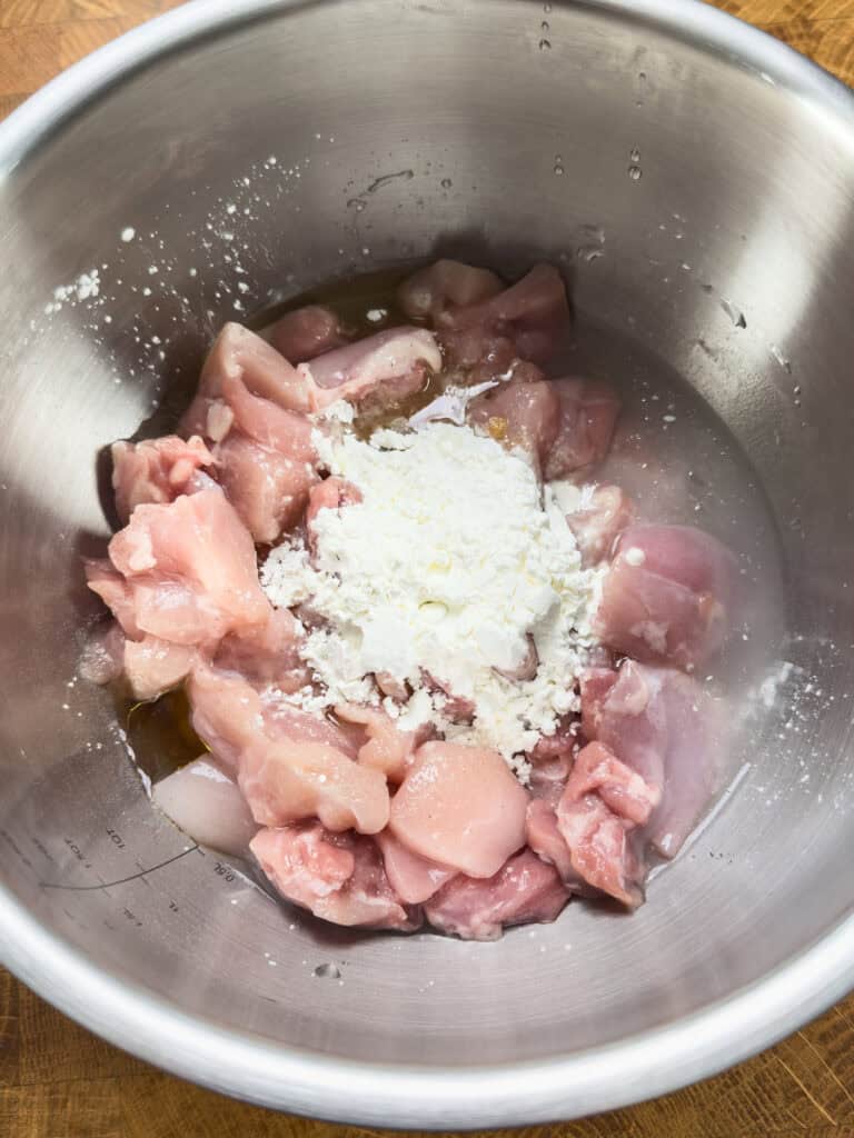 Raw chicken marinating with cornstarch and seasoning in stainless steel bowl
