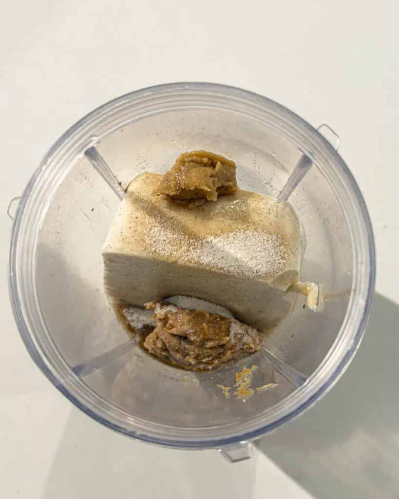 Silken tofu and thick pastes placed inside a blender cup - GENIUS EATS Silken tofu and thick pastes placed inside a blender cup