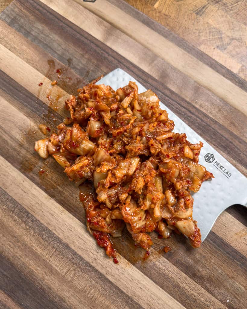 Sliced raw bacon arranged on a wooden cutting board for Kimchi Bacon Pasta preparation