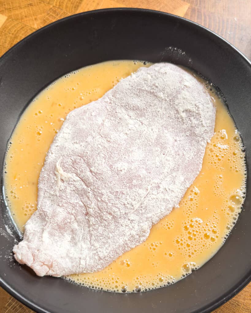 Chicken dipped in beaten egg during breading process