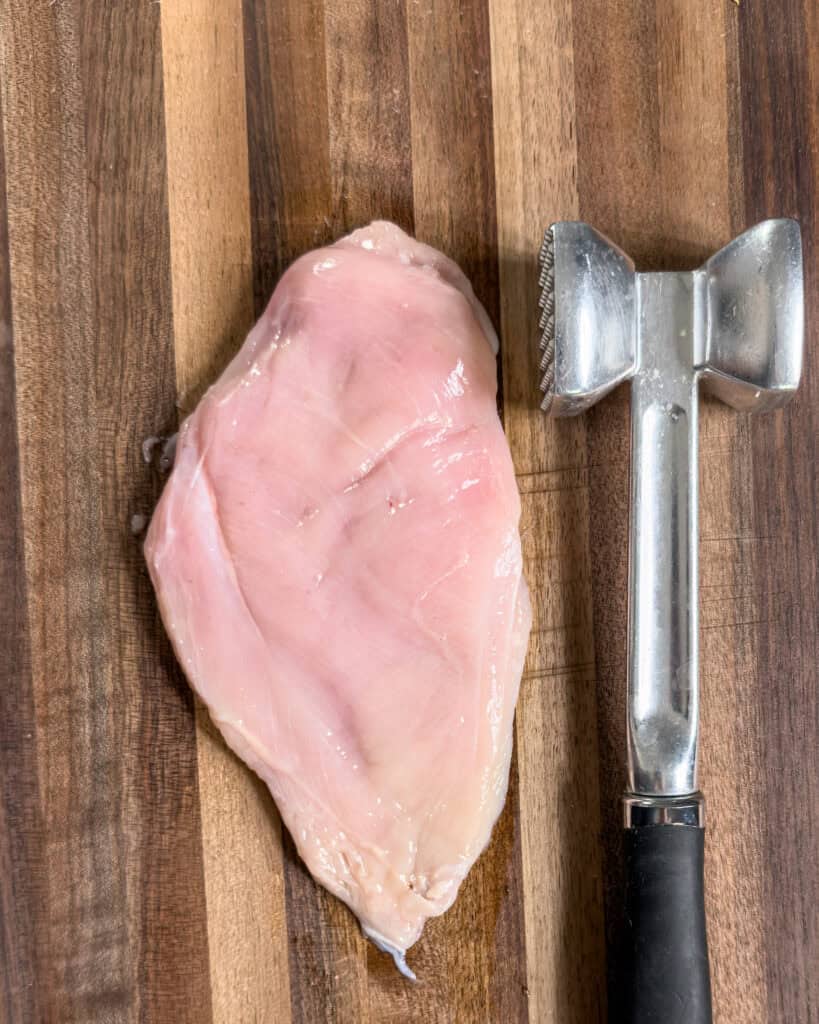 Raw chicken breast with meat tenderizer on cutting board