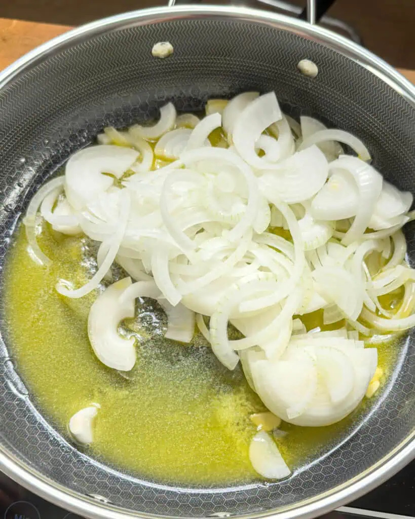 Sliced onions cooking in melted butter in a pan - GENIUS EATS Sliced onions cooking in melted butter in a pan