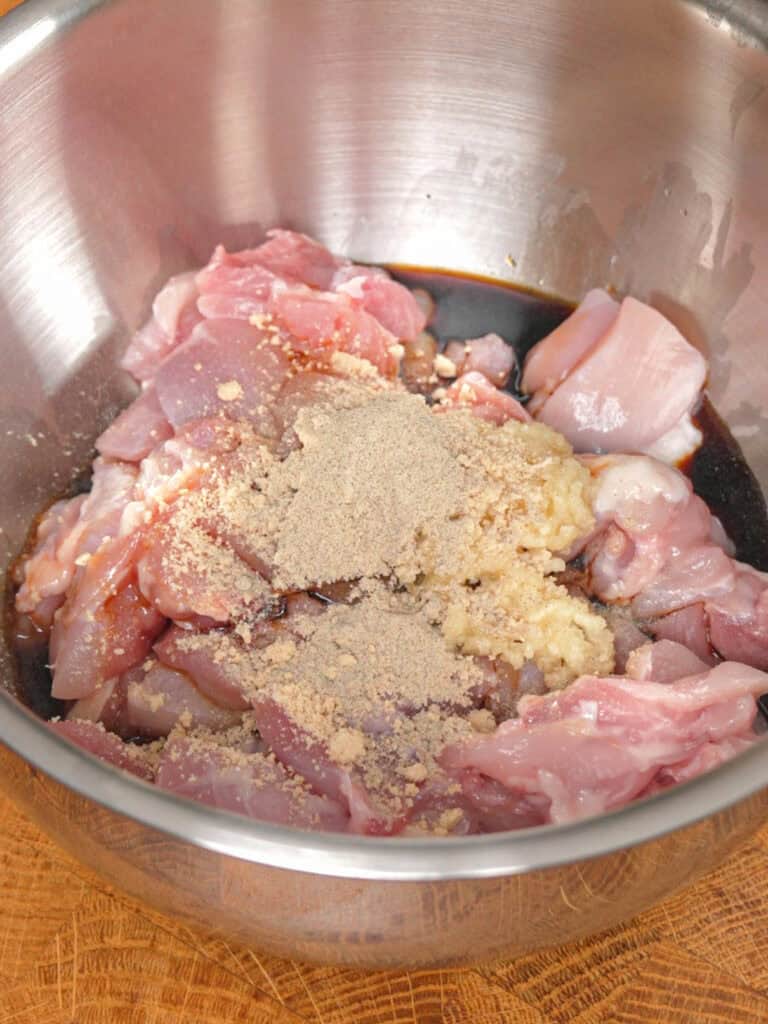 Chicken thighs being coated with soy sauce, seasonings, and garlic for General Tso-Style Chicken Chow Mein marinade.