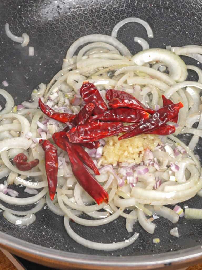 Garlic, onions, and dried chilies stir-frying for General Tso-Style Chicken Chow Mein.