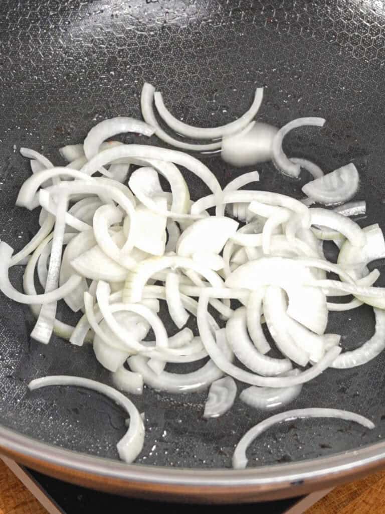 Sliced onions sautéing in a wok for General Tso-Style Chicken Chow Mein