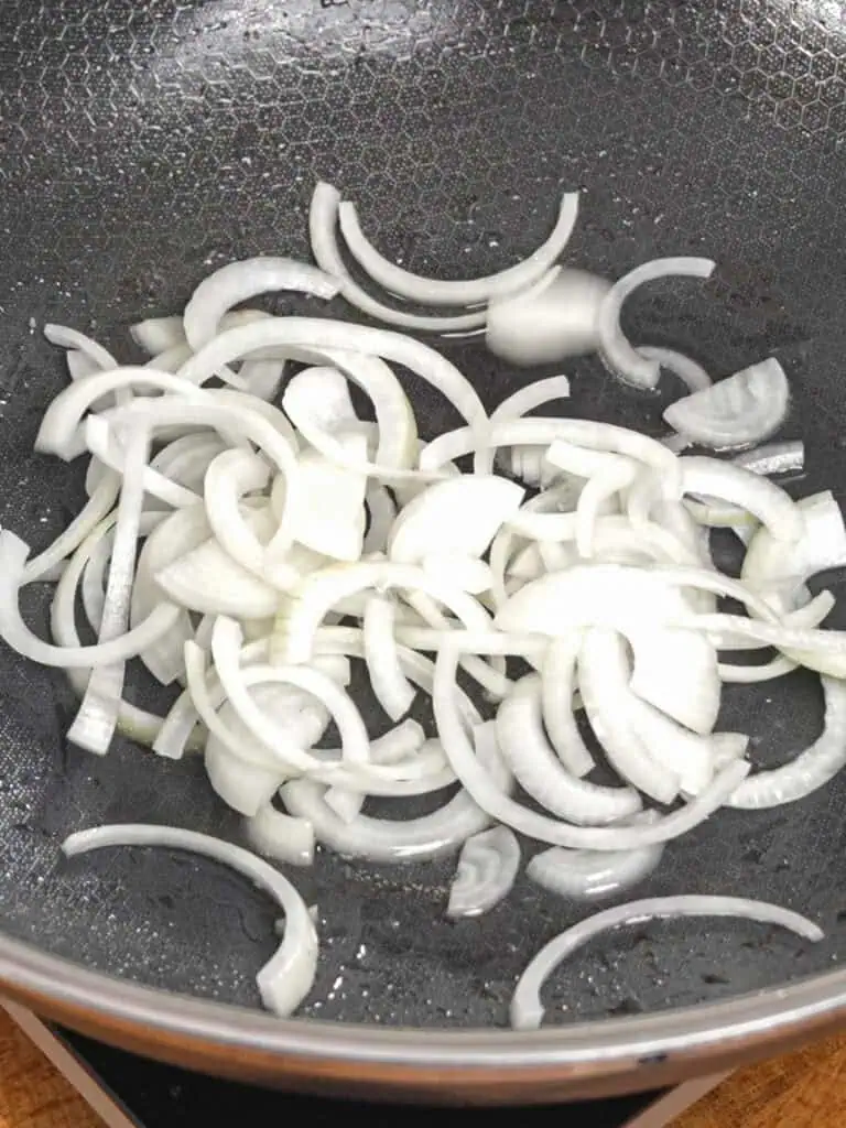 Sliced onions sautéing in a wok for General Tso-Style Chicken Chow Mein - GENIUS EATS Sliced onions sautéing in a wok for General Tso-Style Chicken Chow Mein