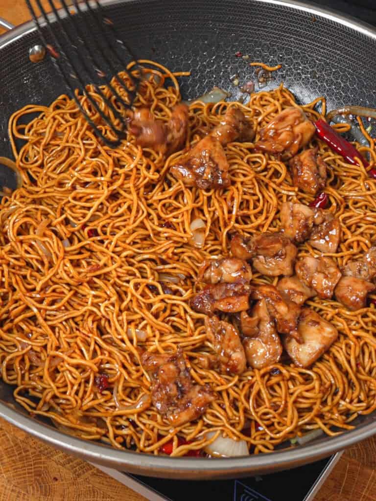 Stir-frying chow mein noodles with cooked chicken and General Tso-style sauce.