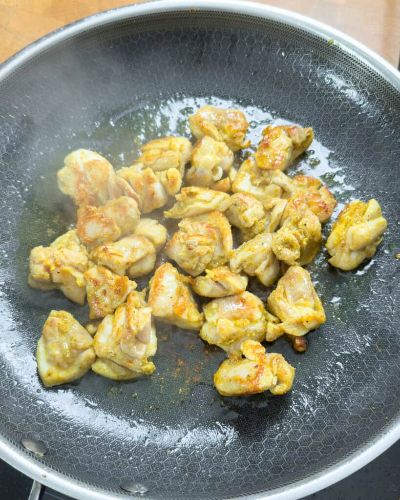 Browned chicken pieces cooking in a pan
