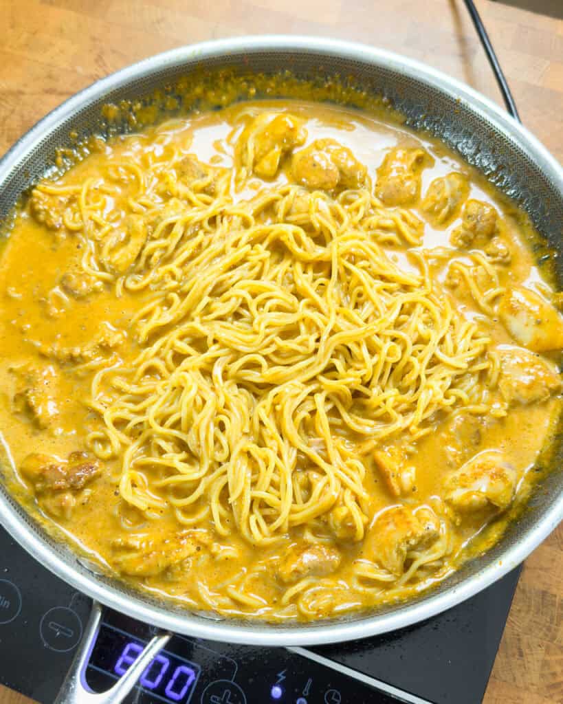 Noodles and chicken mixed in orange curry sauce for Thai red curry chicken ramen