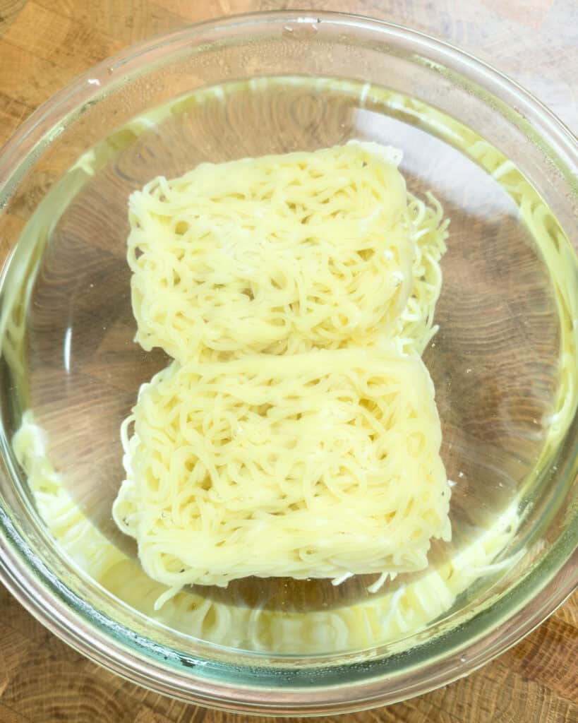 Noodles submerged in clear liquid inside a glass bowl before adding to Thai red curry chicken ramen