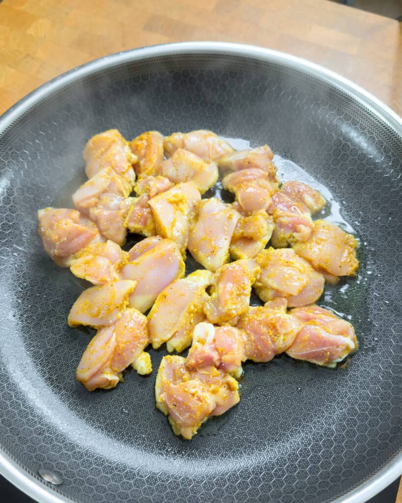 Raw seasoned chicken pieces in a pan with oil