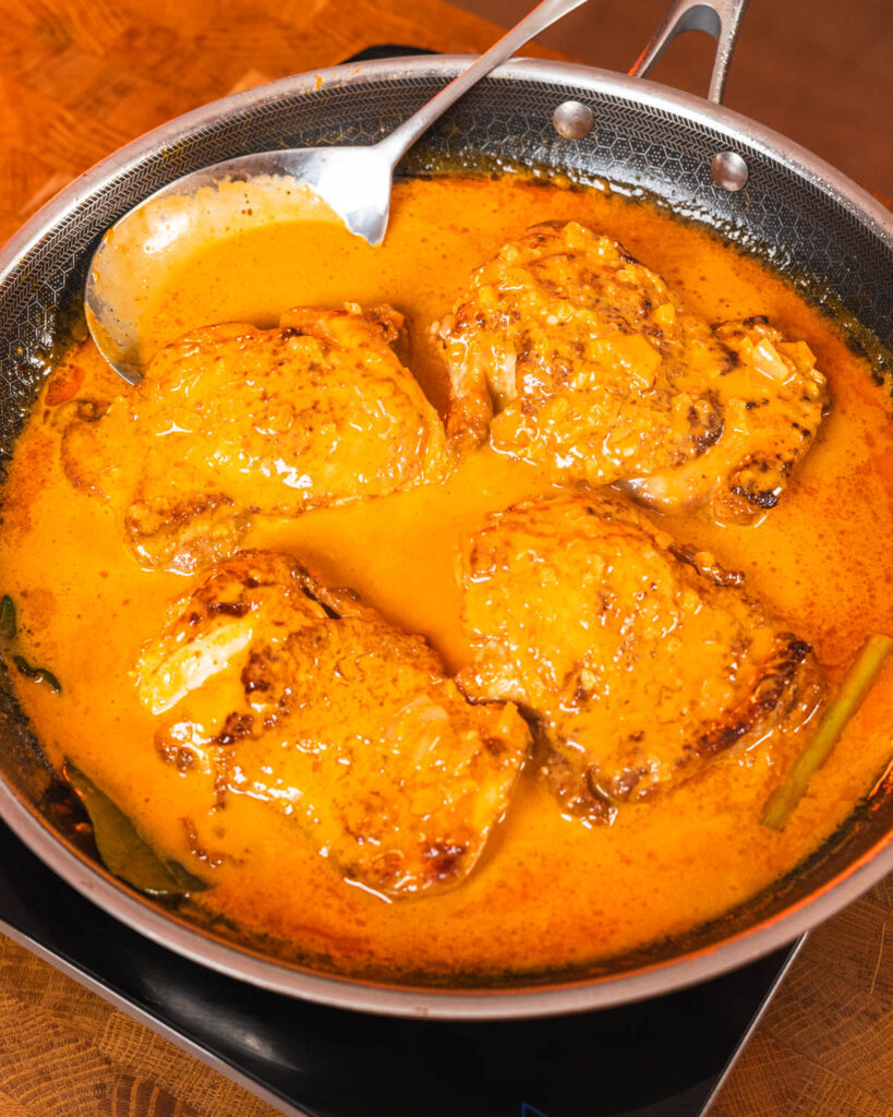 Creamy Gochujang Coconut Chicken pieces in yellow-orange sauce inside a pan - GENIUS EATS Creamy Gochujang Coconut Chicken pieces in yellow-orange sauce inside a pan