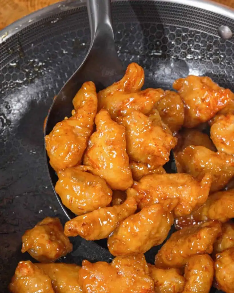Glossy orange Honey Chicken pieces lifted from a pan with a spoon. - GENIUS EATS Glossy orange Honey Chicken pieces lifted from a pan with a spoon.