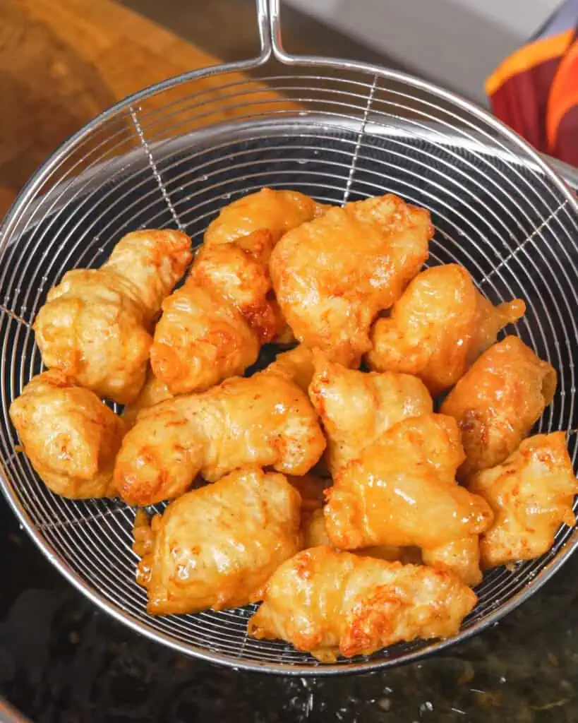 Golden Honey Chicken pieces resting on a wire skimmer after frying. - GENIUS EATS Golden Honey Chicken pieces resting on a wire skimmer after frying.